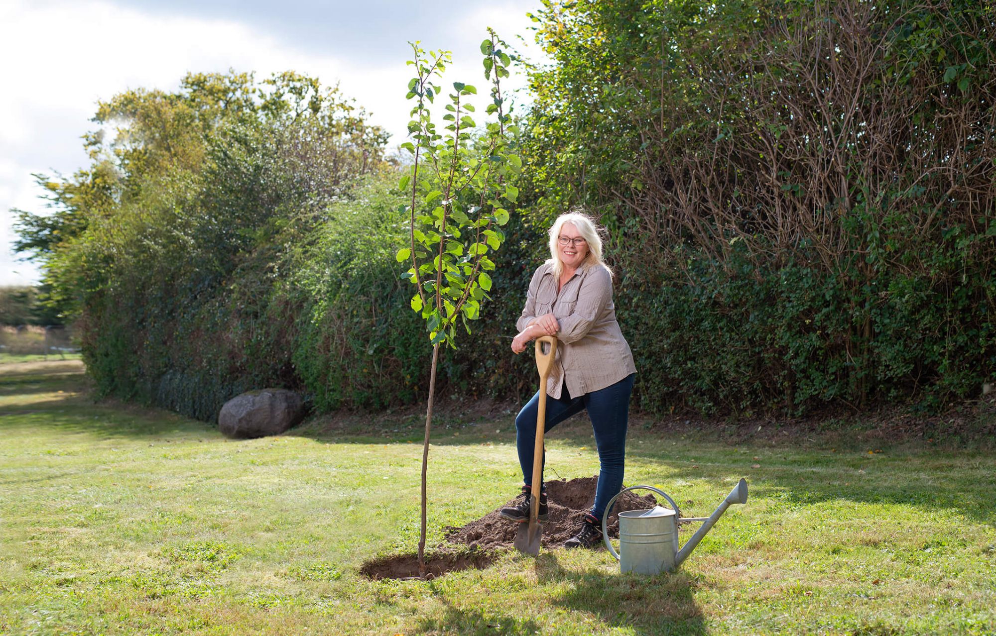 Frau steht stolz vor frisch eingepflanztem Baum